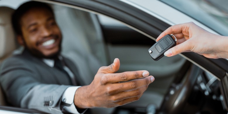a man sitting behind the wheel of a vehicle while a cadillac sales rep hands him the keys.