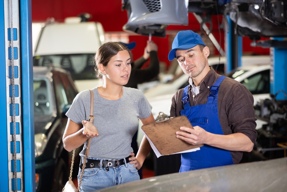 Male car service technician showing a yound woman a clipboard