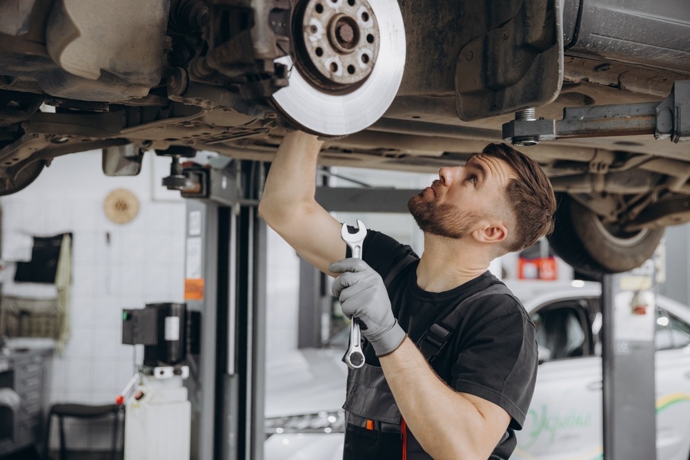 Service technician looking at the under side of a car Service technician looking at the under side of a car