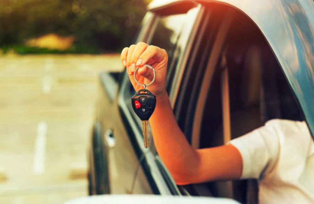 person's hand holding a car key out of a car window