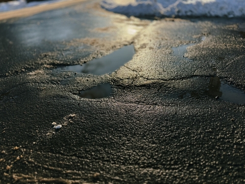 Pothole on a salted winter road, a common cause of wheel bearing wear for Racine drivers